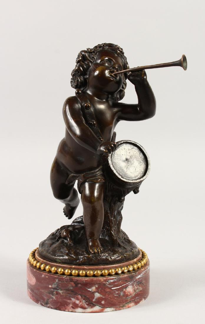 A GOOD SMALL 19TH CENTURY BRONZE CUPID carrying a drum: A GOOD SMALL 19TH CENTURY BRONZE CUPID carrying a drum and blowing a horn, standing on a circular marble base. 9ins high.
