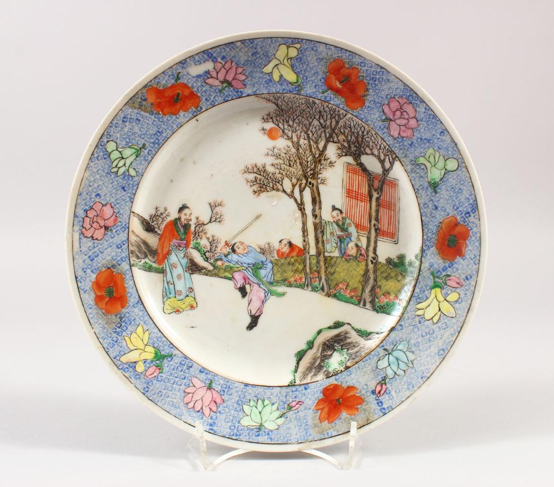 AN EARLY 20TH CENTURY CHINESE FAMILLE ROSE PORCELAIN: AN EARLY 20TH CENTURY CHINESE FAMILLE ROSE PORCELAIN PLATE, painted to its centre with figures in a garden observing a youth wielding a sword, the base with an unusual iron-red archaic dragon enclosed
