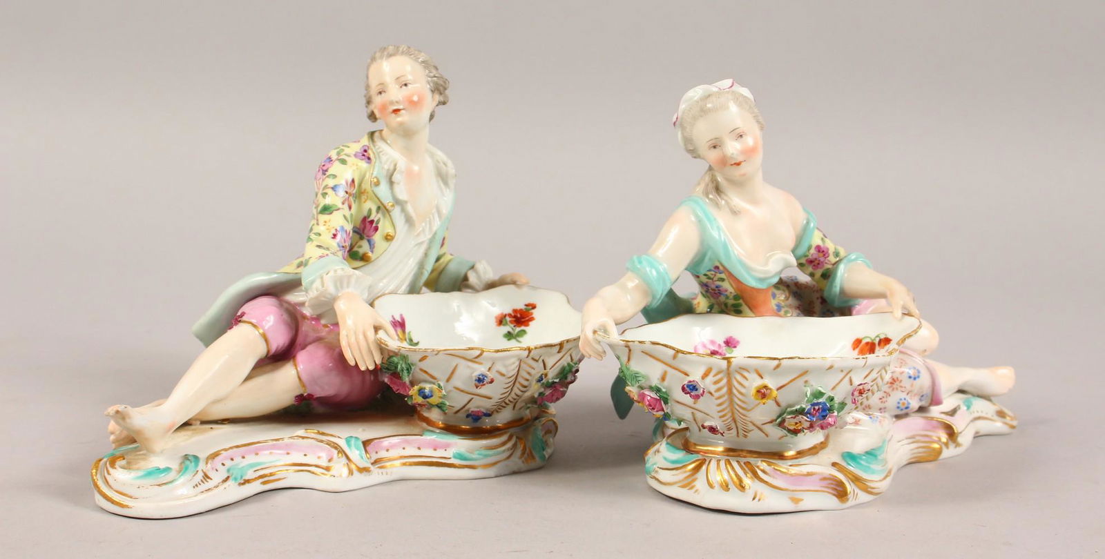 A PAIR OF MEISSEN SWEETMEAT DISHES, with a gallant and: A PAIR OF MEISSEN SWEETMEAT DISHES, with a gallant and lady laying beside a basket. Cross swords mark in blue. Incised 2812. 6.5ins long.