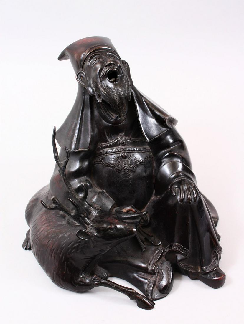 A GOOD JAPANESE MEIJI PERIOD BRONZE OKIMONO OF JUROJIN: A GOOD JAPANESE MEIJI PERIOD BRONZE OKIMONO OF JUROJIN & DEER, the lucky Japanese god in a seated position with his head looking aloft, his deer by his side, 30cm high x 30cm wide.