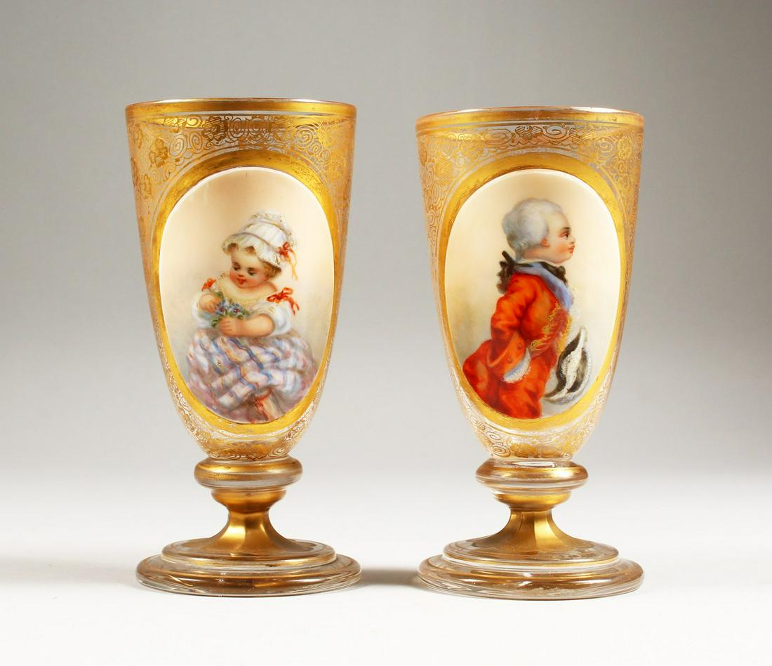 A GOOD PAIR OF 19TH CENTURY GILDED GLASS PEDESTAL: A GOOD PAIR OF 19TH CENTURY GILDED GLASS PEDESTAL GOBLETS, one painted with a three-quarter length portrait of a young boy wearing a red coat, the other a young girl holding a bunch of flowers. 6.5ins
