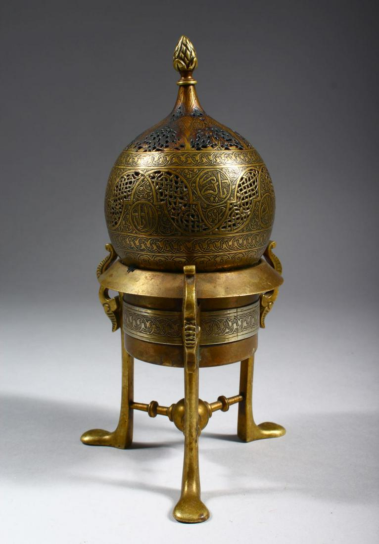 A SYRIAN BRONZE INCENSE BURNER ON STAND, with pierced: A SYRIAN BRONZE INCENSE BURNER ON STAND, with pierced and engraved decoration, the stand with three curving feet, 21cm high.