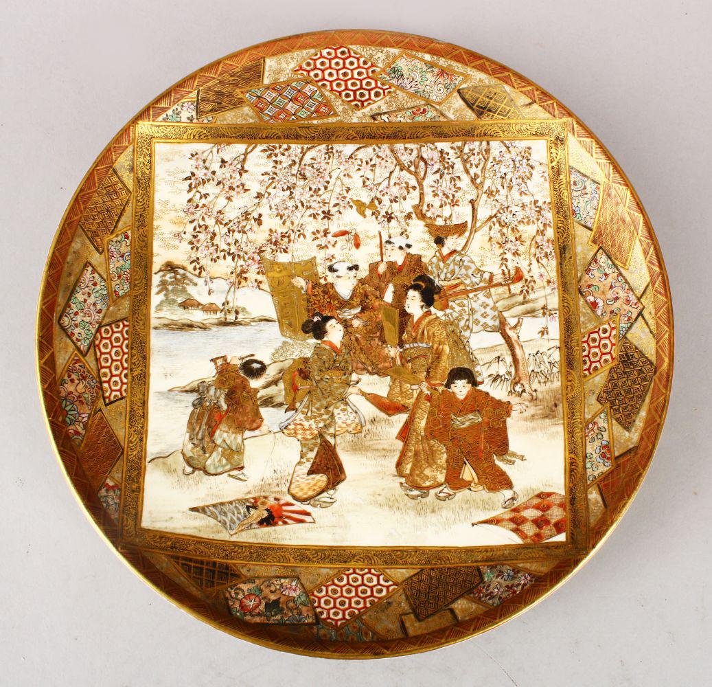 A JAPANESE MEIJI PERIOD SATSUMA PLATE, decorated with a: A JAPANESE MEIJI PERIOD SATSUMA PLATE, decorated with a main panel depicting figures seated in a landscape setting, further decorated with shaped panels of geometric form, the underside with a red sea