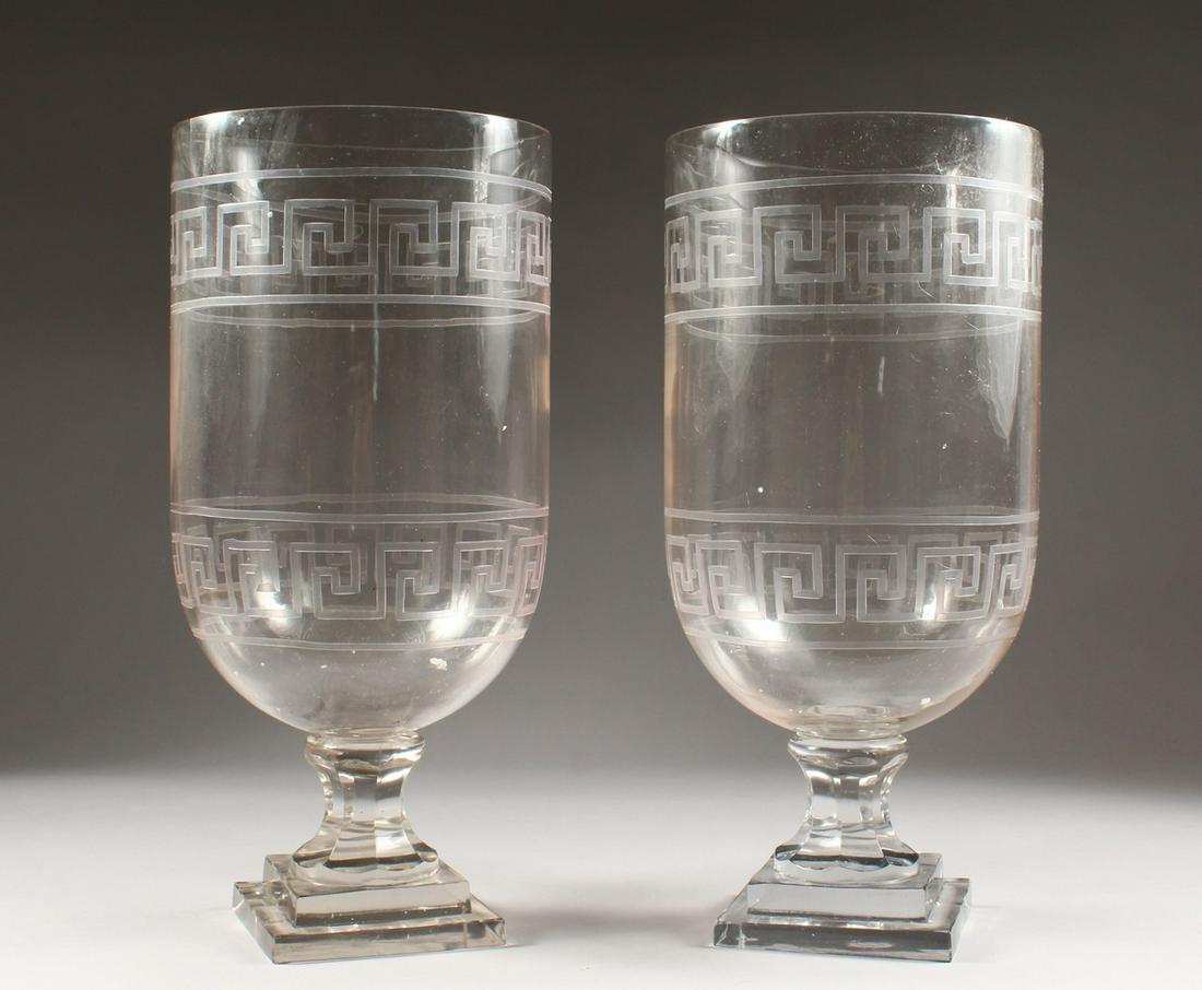A LARGE PAIR OF GLASS URNS, with key pattern: A LARGE PAIR OF GLASS URNS, with key pattern decoration, on a square stepped base.