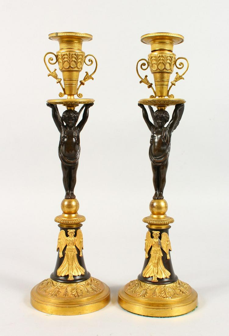 A VERY GOOD PAIR OF EMPIRE THOMAS HOPE DESIGN BRONZE: A VERY GOOD PAIR OF EMPIRE THOMAS HOPE DESIGN BRONZE AND ORMOLU CANDLESTICKS, with winged cupids, on circular bases. 14ins high.