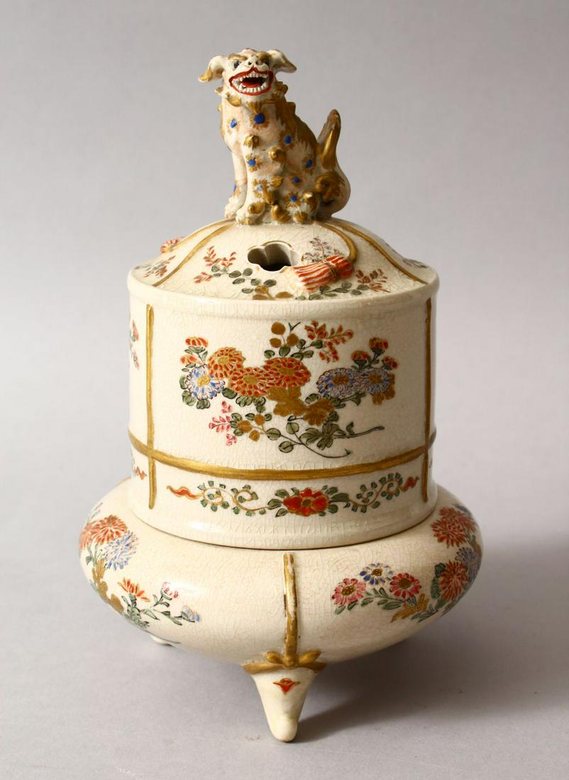 A JAPANESE MEIJI PERIOD SATSUMA SQUAT FORM LIDDED KORO,: A JAPANESE MEIJI PERIOD SATSUMA SQUAT FORM LIDDED KORO, the body of the koro decorated with panels of native flora and gilt borders, on three moulded feet, the cover with a Shi Shi finial, 18cm high. 