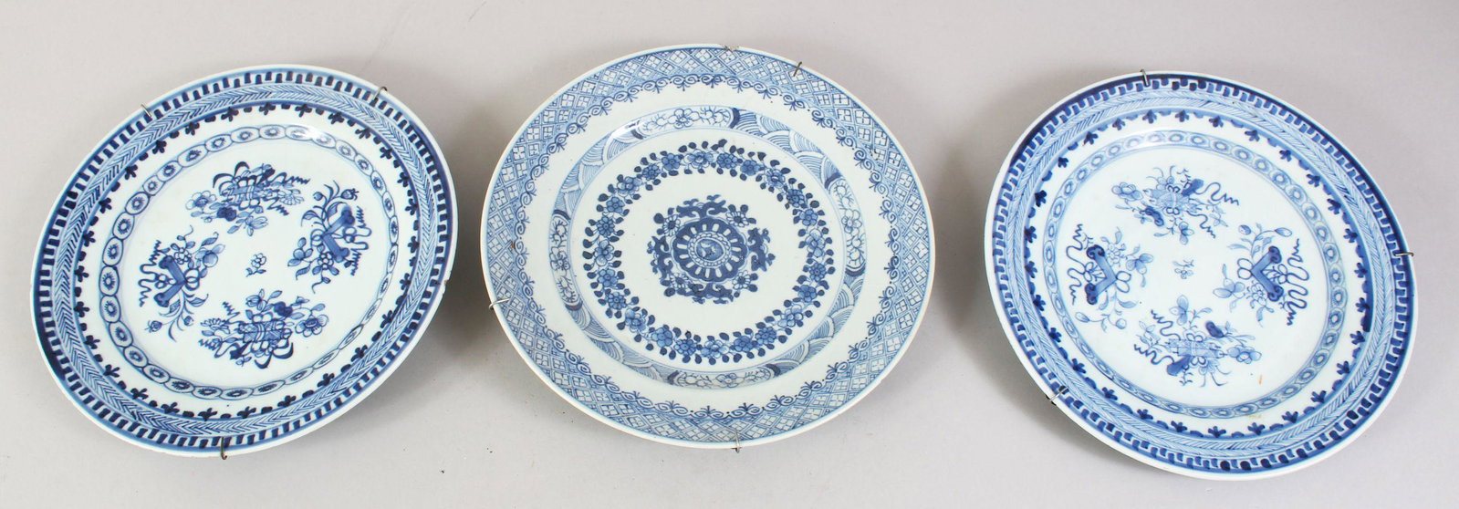 THREE 18TH / 19TH CENTURY CHINESE BLUE & WHITE: THREE 18TH / 19TH CENTURY CHINESE BLUE & WHITE PORCELAIN PLATES, each with floral decoration and a metal wall hanging, 23cm diameter.