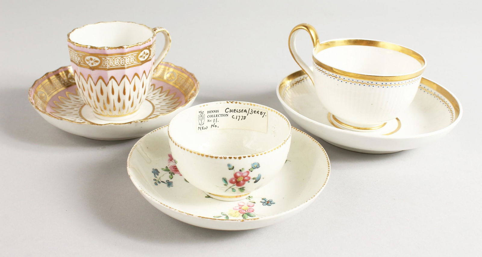 A CHELSEA DERBY FLORAL TEA BOWL AND SAUCER, Dennis: A CHELSEA DERBY FLORAL TEA BOWL AND SAUCER, Dennis Collection, a Derby cup and saucer with tear drop gilding under a pink ground and a Derby moulded teacup and saucer with high handle.