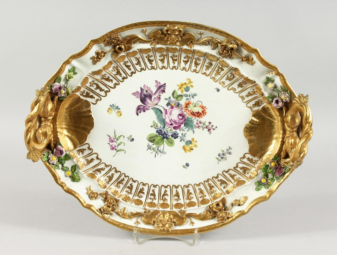 A VERY GOOD MEISSEN OVAL TWO-HANDLED TRAY, with gilt: A VERY GOOD MEISSEN OVAL TWO-HANDLED TRAY, with gilt entwined dolphin handle, the border with flowers in relief, encrusted and painted with flowers. Cross swords mark in blue. 16ins long.