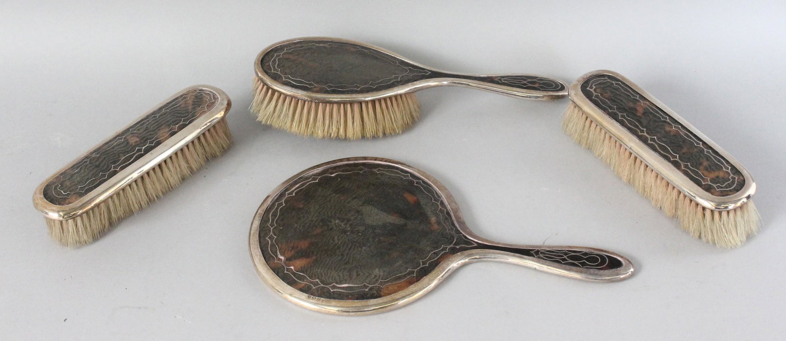 A SILVER AND TORTOISESHELL HAND MIRROR AND THREE: A SILVER AND TORTOISESHELL HAND MIRROR AND THREE BRUSHES. Birmingham 1919. Maker: LS for LEVI & SALAMAN.