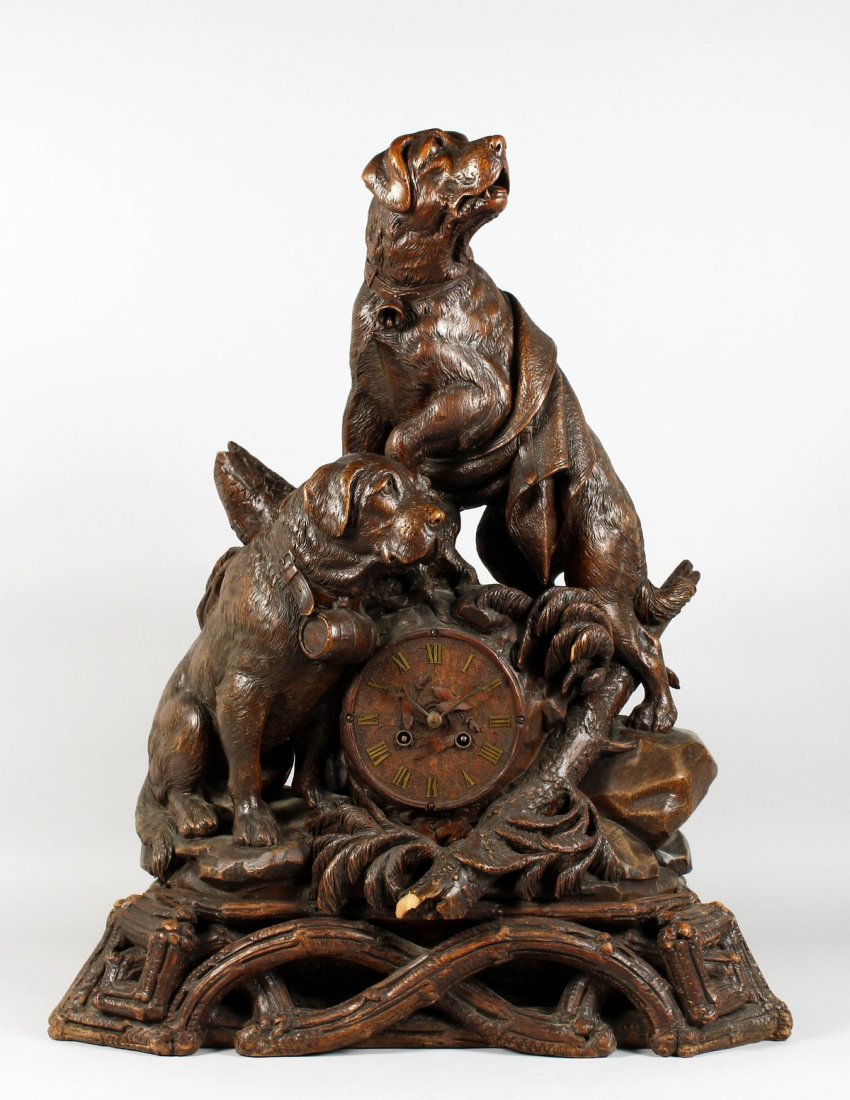 A BLACK FOREST CLOCK CARVED WITH TWO ST BERNARD DOGS: A VERY GOOD ANTIQUE BLACK FOREST CLOCK CARVED WITH TWO SAINT BERNARD DOGS, one with a bell around his neck and a blanket across its back, the other a barrel, the five inch dial striking on a single be