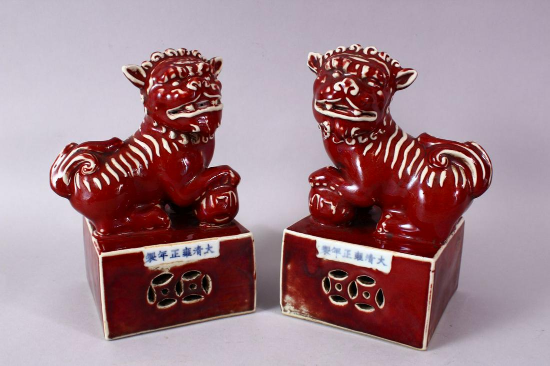 A PAIR OF CHINESE COPPER RED PORCELAIN TEMPLE LIONS,: A PAIR OF CHINESE COPPER RED PORCELAIN TEMPLE LIONS, each posed upon a fixed base with their paw upon a ball, the bases with openwork and a six character mark, 21cm high x 15cm wide,