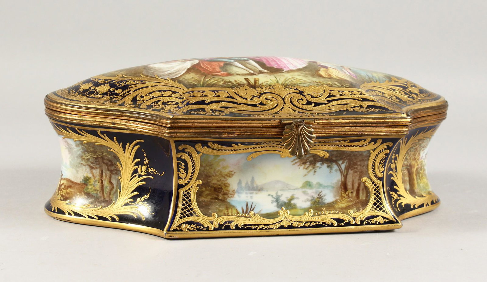 A VERY GOOD FRENCH SEVRES DESIGN BLUE AND GILT: A VERY GOOD FRENCH SEVRES DESIGN BLUE AND GILT PORCELAIN BOX AND COVER, the top painted with a design, figures by a lake, four vignettes to the sides, the interior white and painted with flowers with 