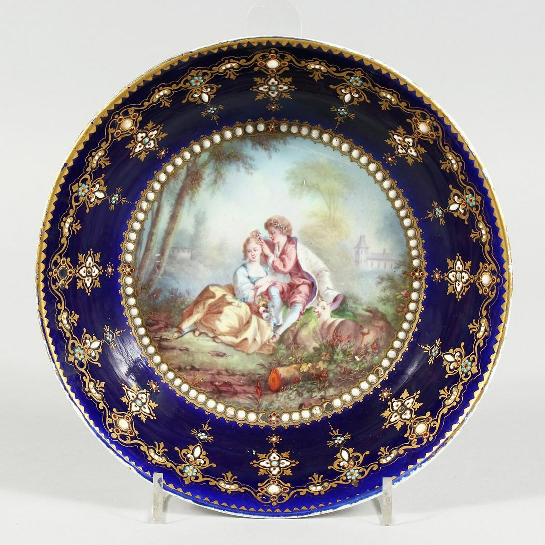 AN 18TH CENTURY SEVRES PORCELAIN CIRCULAR DEEP DISH: AN 18TH CENTURY SEVRES PORCELAIN CIRCULAR DEEP DISH rich blue ground, pearl work, the centre painted with young lovers and goat. Sevres mark in blue ,8ins diameter.