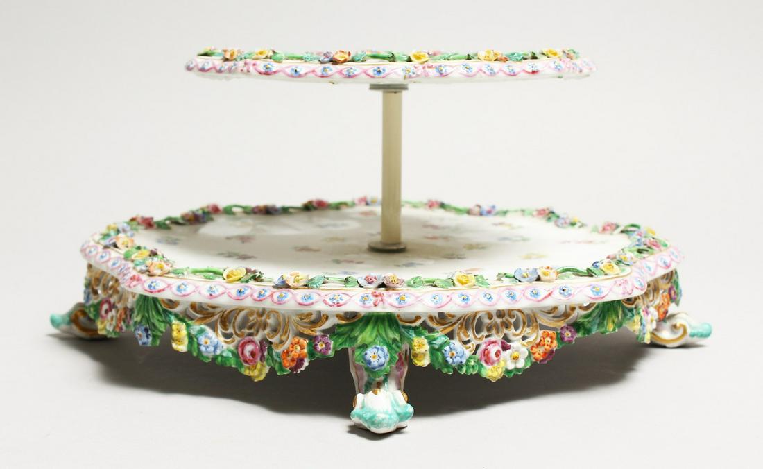 A 19TH CENTURY MEISSEN PORCELAIN TWO TIER STAND painted: A 19TH CENTURY MEISSEN PORCELAIN TWO TIER STAND painted with roses and encrusted with flowers. Cross swords mark in blue, 5.5ins high.