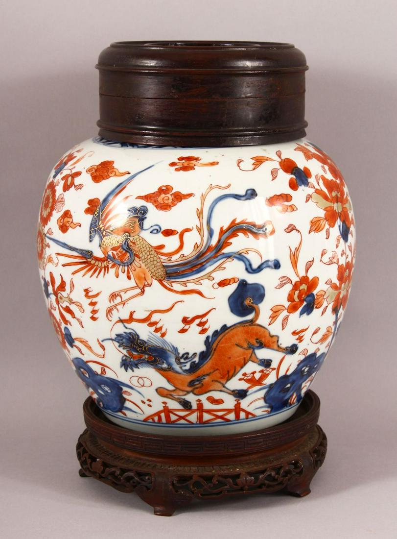 A 18TH / 19TH CENTURY CHINESE IMARI PORCELAIN GINGER: A 18TH / 19TH CENTURY CHINESE IMARI PORCELAIN GINGER JAR & WOOD COVER - decorated in typical imari palate depicting flora, with a carved wooden stand and cover, 32cm high overall.