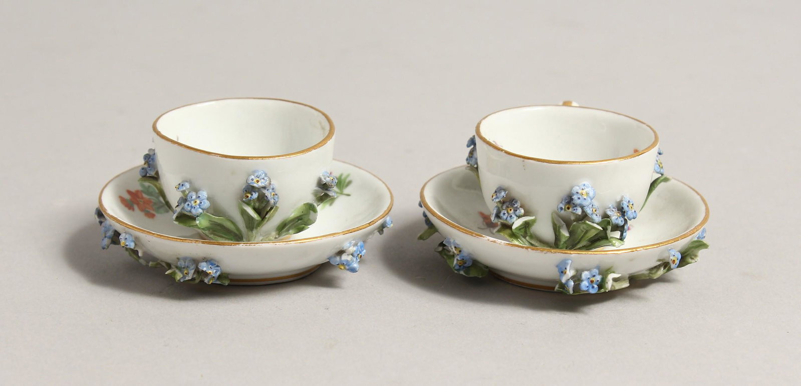 A MINIATURE PAIR OF 19TH CENTURY MEISSEN ENCRUSTED CUPS: A MINIATURE PAIR OF 19TH CENTURY MEISSEN ENCRUSTED CUPS AND SAUCERS. Cross swords mark in blue.