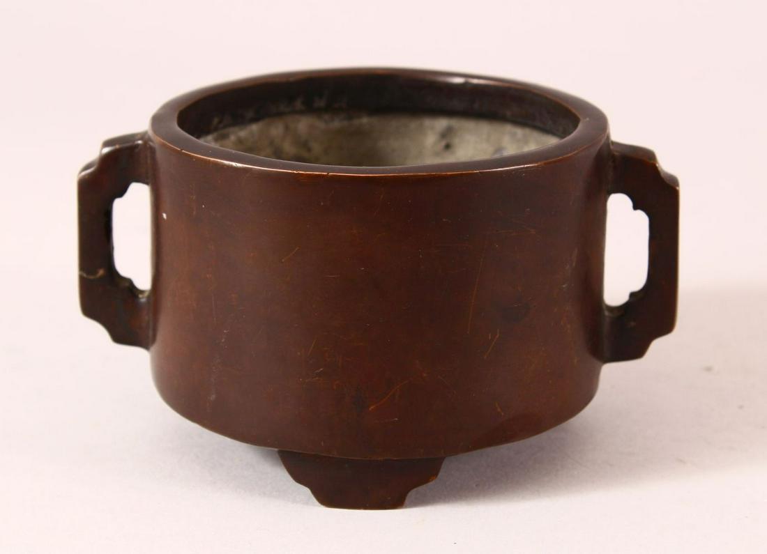 A CHINESE BRONZE TWIN HANDLED CENSER, on three feet: A CHINESE BRONZE TWIN HANDLED CENSER, on three feet with an impressed seal mark to base, 14cm diameter.