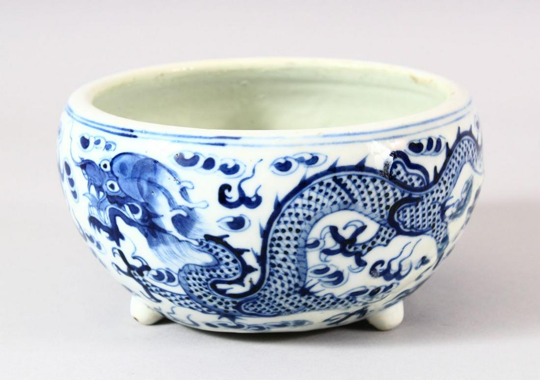 A CHINESE BLUE & WHITE PORCELAIN DRAGON BRUSH POT -: A CHINESE BLUE & WHITE PORCELAIN DRAGON BRUSH POT - with tripod feet, depicting dragons chasing the pearl, AF - restored , 17cm