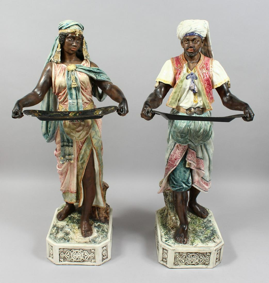 A VERY GOOD PAIR OF LARGE MAJOLICA POTTERY FIGURES OF AN ARAB MAN AND YOUNG GIRL standing holding: A VERY GOOD PAIR OF LARGE MAJOLICA POTTERY FIGURES OF AN ARAB MAN AND YOUNG GIRL standing holding toleware trays and standing on rectangular bases. No. 2119, 29ins high.