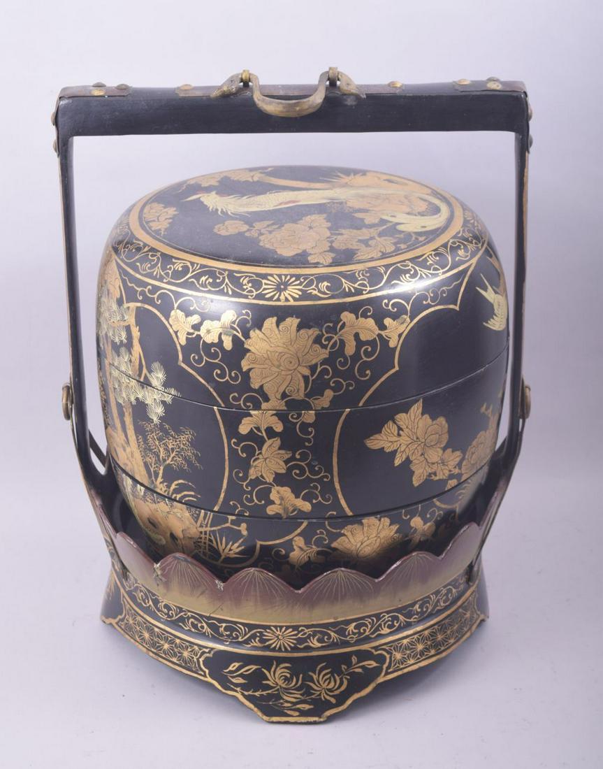 AN EARLY 20TH CENTURY LACQUERED WOOD JUBAKO / FOOD CARRIER, in black and gilt lacquer and decorated: AN EARLY 20TH CENTURY LACQUERED WOOD JUBAKO / FOOD CARRIER, in black and gilt lacquer and decorated with panels of native flora and fourna, the barrel formed box in three opening sections and supporte