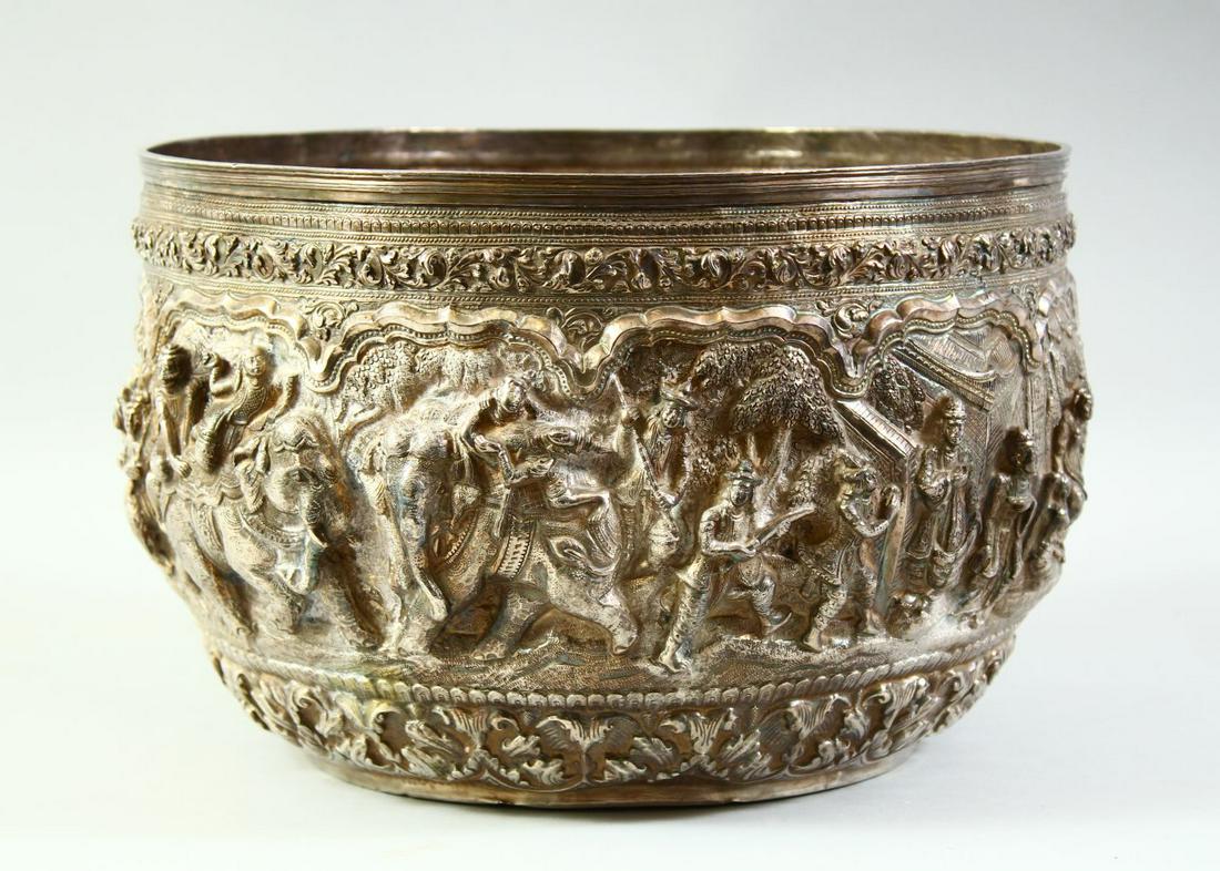 A LARGE BURMESE EMBOSSED AND CHASED SILVER BOWL, with raised decoration of figural scenes and: A LARGE BURMESE EMBOSSED AND CHASED SILVER BOWL, with raised decoration of figural scenes and animals within a floral lambrequin border, 32cm diameter.