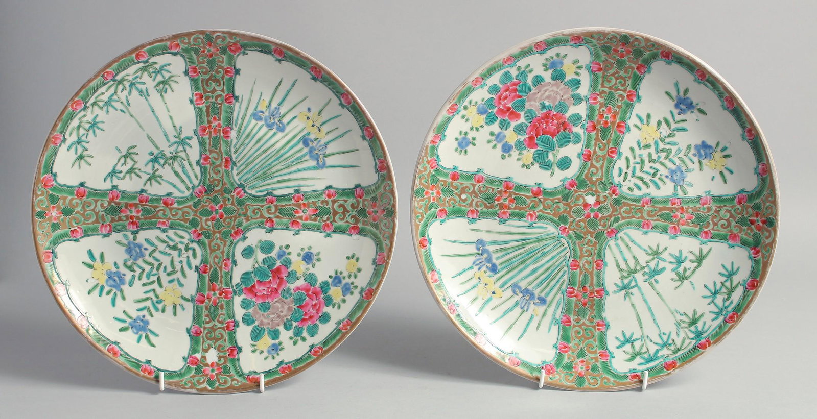 A PAIR OF CHINESE CANTON FAMILLE ROSE PORCELAIN PLATES, each painted with panels of native flora,: A PAIR OF CHINESE CANTON FAMILLE ROSE PORCELAIN PLATES, each painted with panels of native flora, each with painted red inscription to base and impressed mark, 30.5cm diameter.