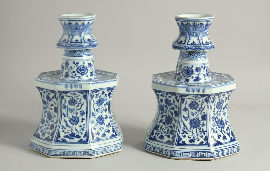 A PAIR OF CHINESE BLUE AND WHITE PORCELAIN CANDLESTICKS each painted with panels of flora and other: A PAIR OF CHINESE BLUE AND WHITE PORCELAIN CANDLESTICKS each painted with panels of flora and other motifs, bearing a four-character mark. 26.5cm high