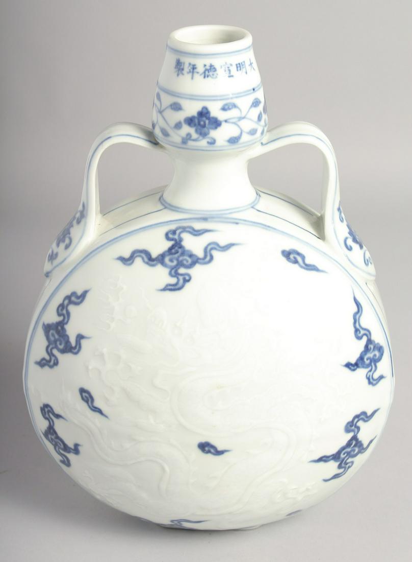 A CHINESE BLUE AND WHITE PORCELAIN TWIN HANDLED MOON FLASK with carved central dragon. 29.5cm high: A CHINESE BLUE AND WHITE PORCELAIN TWIN HANDLED MOON FLASK with carved central dragon. 29.5cm high