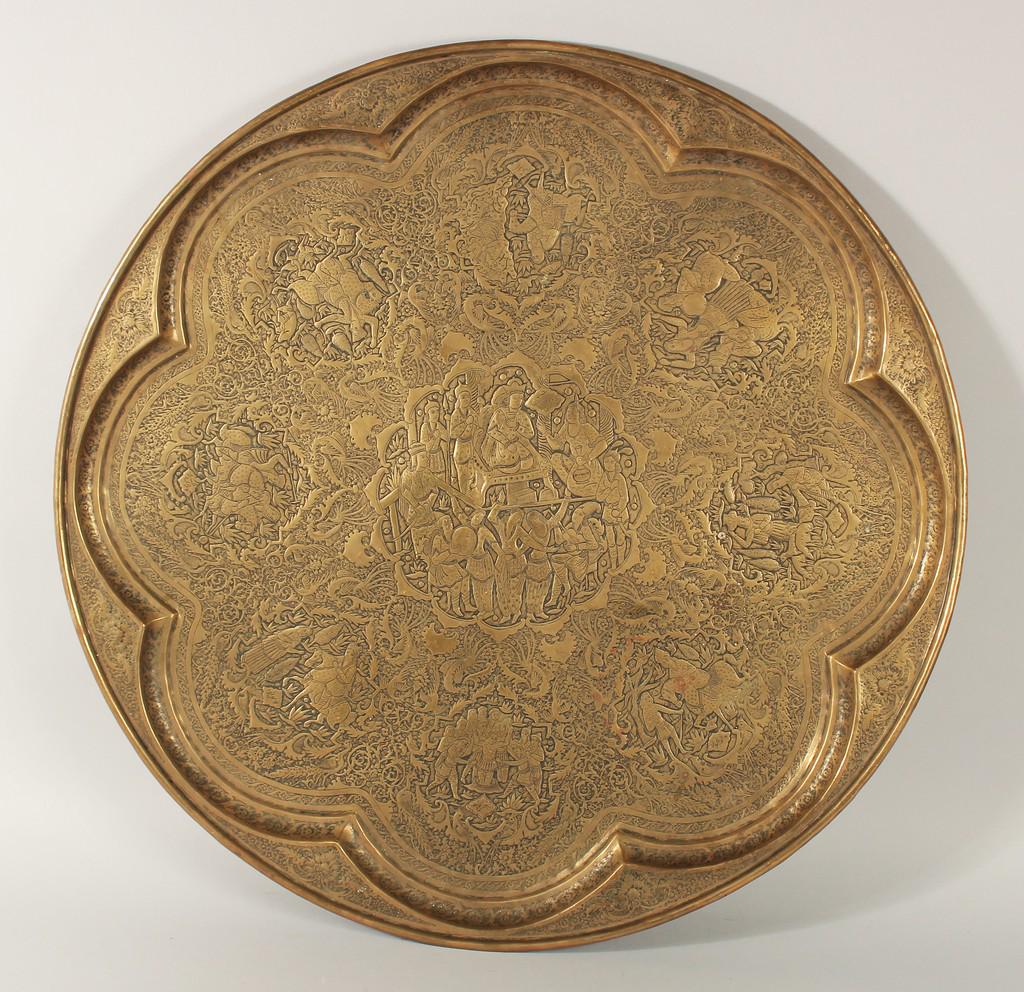 A LARGE ISLAMIC ENGRAVED BRASS TRAY, finely engraved with panels of figures on a foliate background,: A LARGE ISLAMIC ENGRAVED BRASS TRAY, finely engraved with panels of figures on a foliate background, 68cm diameter.