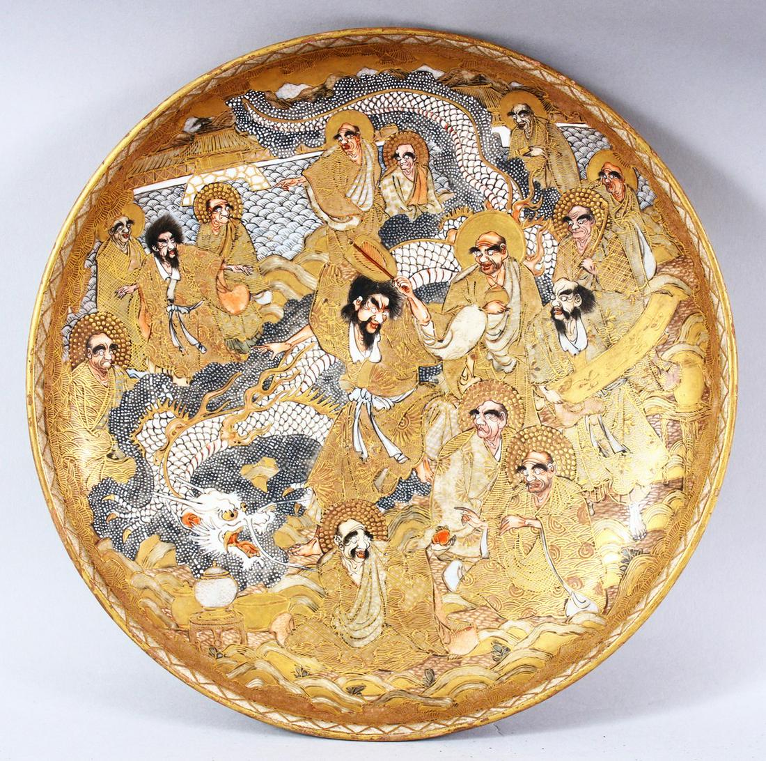 A GOOD JAPANESE SATSUMA PORCELAIN DISH, painted with various figures / deities in gilt and a white: A GOOD JAPANESE SATSUMA PORCELAIN DISH, painted with various figures / deities in gilt and a white dragon, 24cm high.