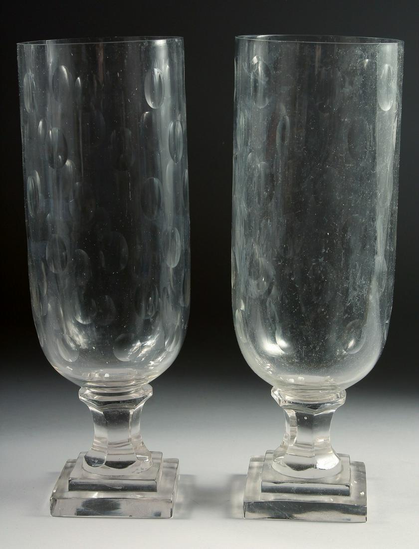 A SMALL PAIR OF GLASS STORM - HURRICANE LAMPS on square bases. 13ins high.: A SMALL PAIR OF GLASS STORM - HURRICANE LAMPS on square bases. 13ins high.