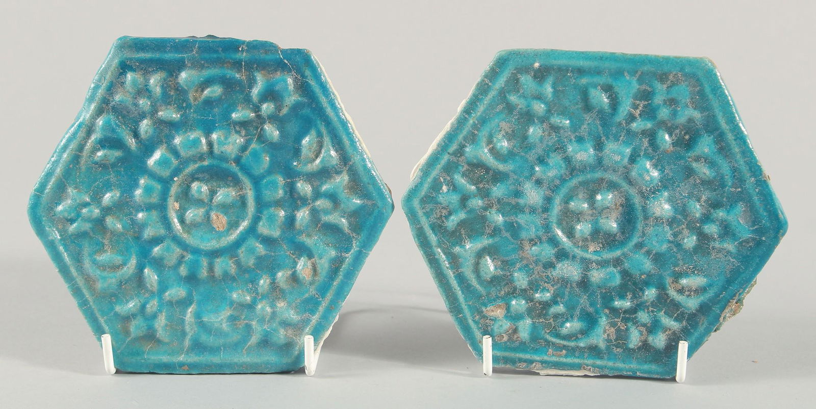 A PAIR OF 13TH CENTURY PERSIAN SELJUK GLAZED POTTERY HEXAGONAL TILES, with raised floral motif: A PAIR OF 13TH CENTURY PERSIAN SELJUK GLAZED POTTERY HEXAGONAL TILES, with raised floral motif decoration, 14cm at widest point.