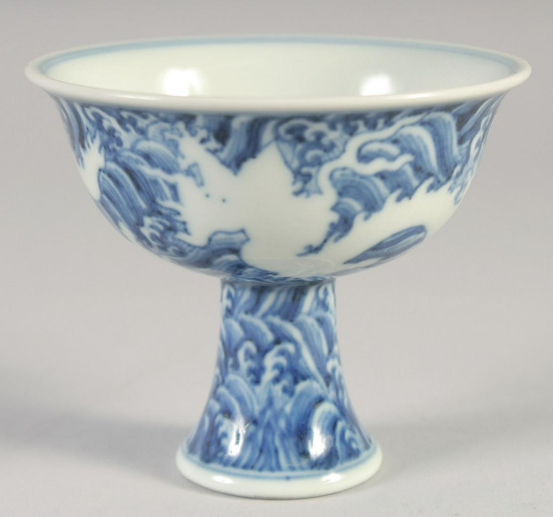 A CHINESE BLUE AND WHITE PORCELAIN STEM CUP, with white dragons and waves, bearing six-character: A CHINESE BLUE AND WHITE PORCELAIN STEM CUP, with white dragons and waves, bearing six-character mark, 10cm diameter.