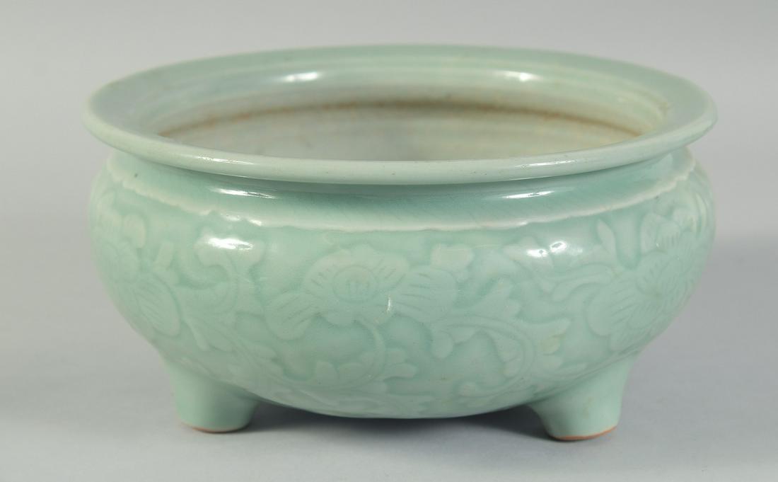 A 19TH CENTURY CHINESE CELADON GLAZE PORCELAIN BOWL / CENSER, with carved floral decoration to the: A 19TH CENTURY CHINESE CELADON GLAZE PORCELAIN BOWL / CENSER, with carved floral decoration to the sides, raised on three feet, 21.5cm diameter.