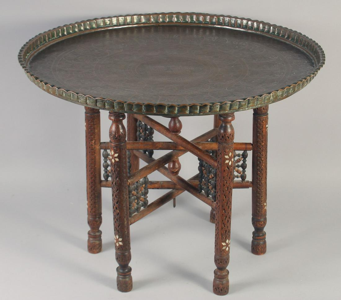 A LARGE 19TH CENTURY PERSIAN BRASS TRAY TABLE, the tray engraved with panels of figures, with mother: A LARGE 19TH CENTURY PERSIAN BRASS TRAY TABLE, the tray engraved with panels of figures, with mother of pearl inlaid wooden stand, tray 70.5cm diameter.