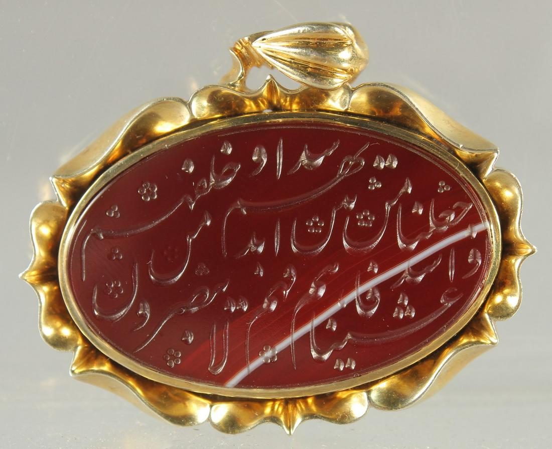 A FINE ISLAMIC CALLIGRAPHIC RED STONE SEAL inset within a gilt metal pendant, stamped to the verso, (1 of 2)