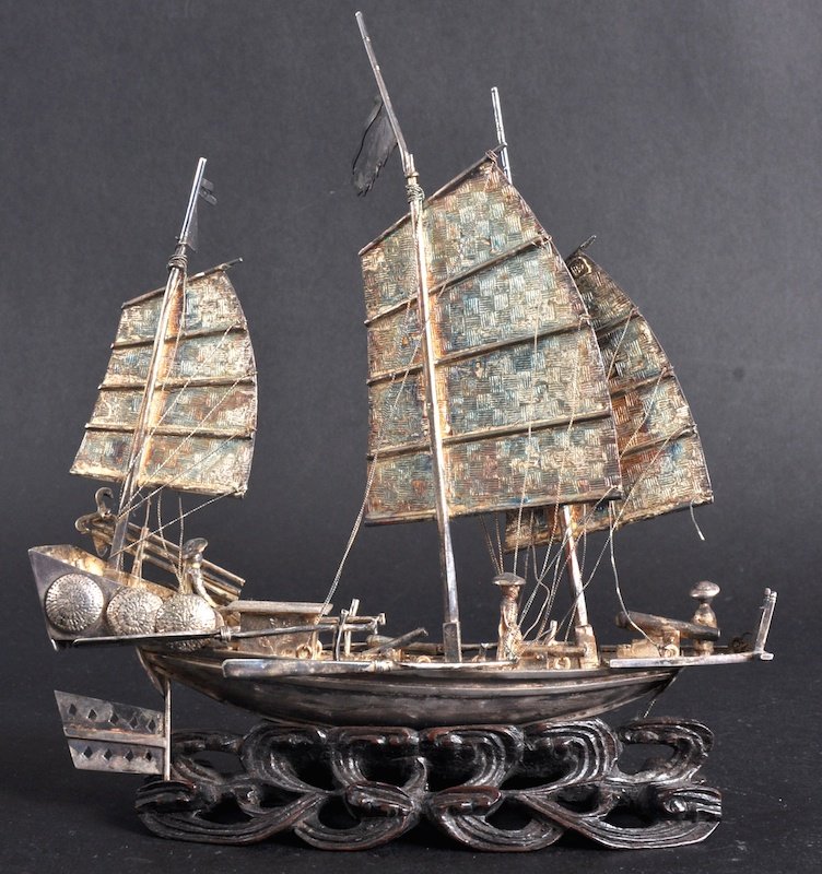 A 19TH CENTURY CHINESE SILVER JUNK BOAT modelled: A 19TH CENTURY CHINESE SILVER JUNK BOAT modelled with attendants, upon a hardwood base. Signed. Minor faults.5.75ins wide.