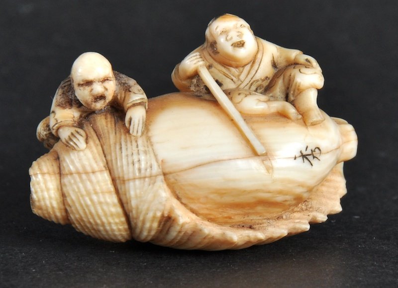 A LATE 19TH CENTURY JAPANESE IVORY NETSUKE in the: A LATE 19TH CENTURY JAPANESE IVORY NETSUKE in the form of a nut with two figures surmounting it. Signed. Natural flaws.1.25ins wide.