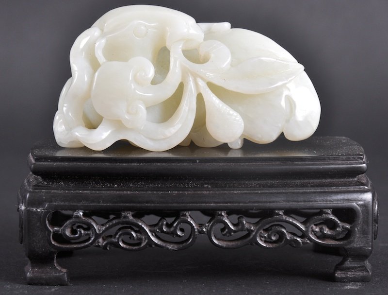 AN EARLY 20TH CENTURY CHINESE WHITE JADE CARVED F: AN EARLY 20TH CENTURY CHINESE WHITE JADE CARVED FIGURE OF A RAM modelled recumbent, holding a lotus flower in its mouth. Natural fissures. 2. 75ins wide.