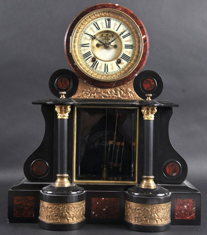 A VICTORIAN BLACK SLATE AND RED MARBLE MANTLE CL: A VICTORIAN BLACK SLATE AND RED MARBLE MANTLE CLOCK with enamel dial, inset with gilded plaques of classical figures on horseback. 17. 75ins high.