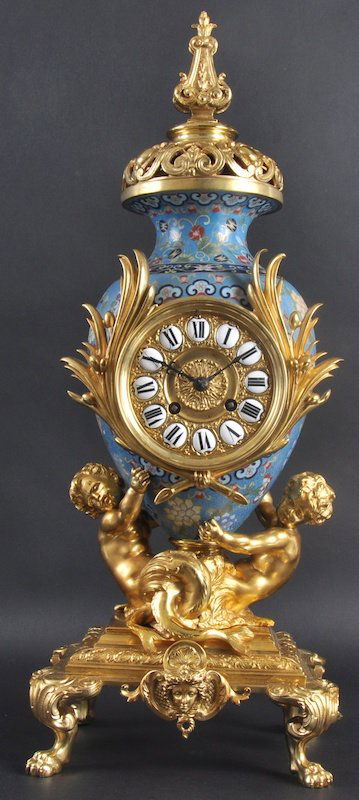 A LATE 19TH CENTURY FRENCH ORMOLU AND CHAMPLEVE: A LATE 19TH CENTURY FRENCH ORMOLU AND CHAMPLEVE ENAMEL MANTLE CLOCK of urn shape, decorated with foliage, supported with two putti to the base, upon paw feet. 21ins high.