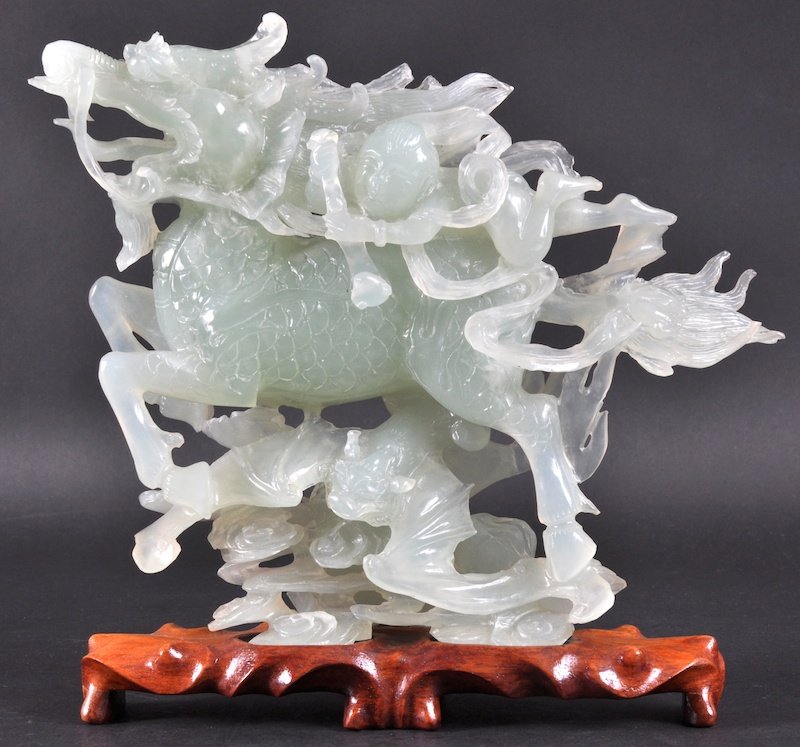 A CHINESE CARVED GREEN JADE FIGURE OF A DRAGON mod: A CHINESE CARVED GREEN JADE FIGURE OF A DRAGON modelled with a young attendant. Minor nicks. 9. 25ins wide.