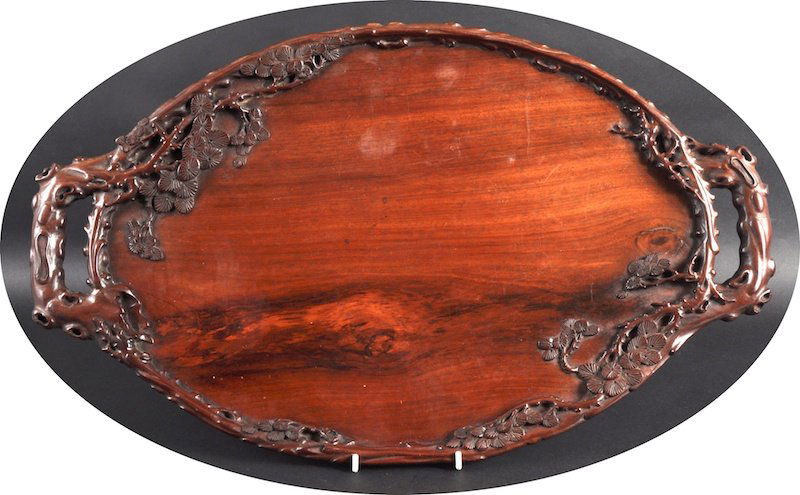 A 19TH CENTURY CHINESE CARVED HARDWOOD TWIN HANDL: A 19TH CENTURY CHINESE CARVED HARDWOOD TWIN HANDLED TRAY possibly Huanghuali, of naturalistic form with flowering pine trees. 1ft 11ins wide.