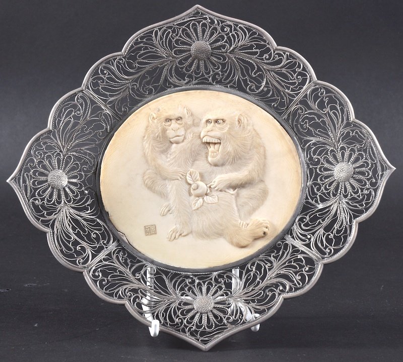 A 19TH CENTURY JAPANESE MEIJI PERIOD IVORY AND SI: A 19TH CENTURY JAPANESE MEIJI PERIOD IVORY AND SILVER DISH the ivory panel carved with two monkeys, within a pierced filigree frame. Nicks to ivory rim.7.75ins wide.