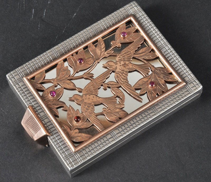 A SILVER AND GOLD BOUCHERON COMPACT, the silver b: A SILVER AND GOLD BOUCHERON COMPACT, the silver body with engine turned decoration, then front gold pierced panel of birds within leaves set with cabochon rubies.