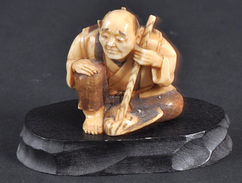 A CARVED IVORY NETSUKE OF A MAN KNEELING WITH A ST: A CARVED IVORY NETSUKE OF A MAN KNEELING WITH A STAFF.