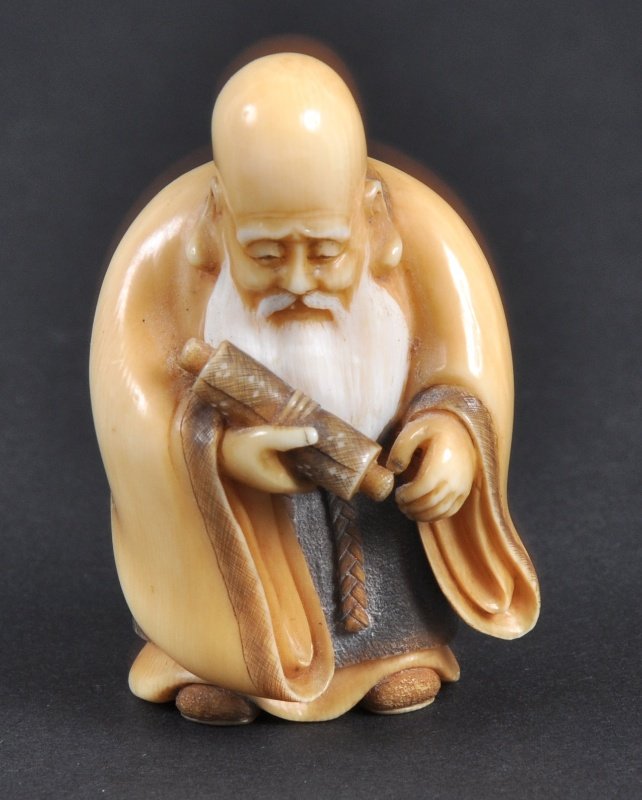 A CARVED IVORY NETSUKE OF A MAN WITH A SCROLL. : A CARVED IVORY NETSUKE OF A MAN WITH A SCROLL.