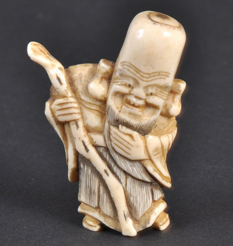 A CARVED IVORY NETSUKE OF A MAN WITH A STAFF. : A CARVED IVORY NETSUKE OF A MAN WITH A STAFF.