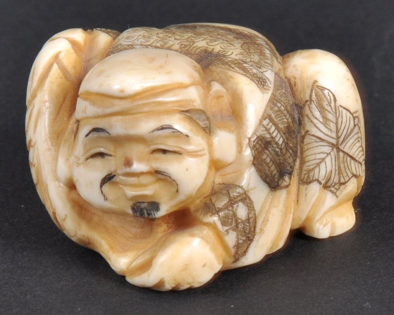 A CARVED IVORY NETSUKE OF A MAN CROUCHING OVER. : A CARVED IVORY NETSUKE OF A MAN CROUCHING OVER.